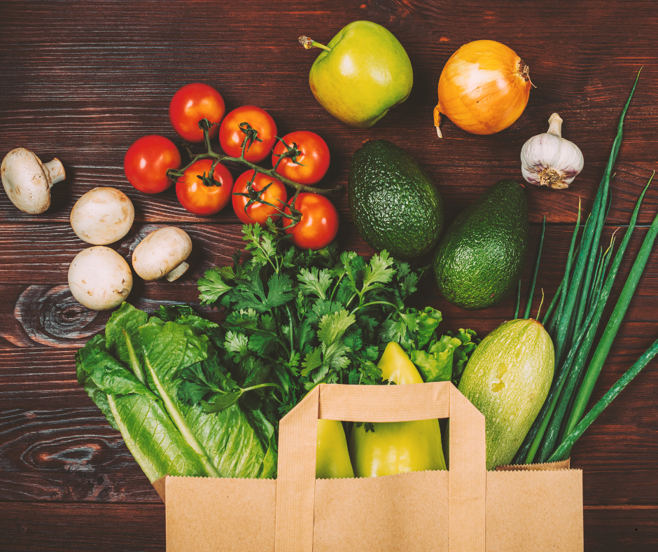 Fresh fruit and vegetables spilling out of a paper shopping bag onto a table.